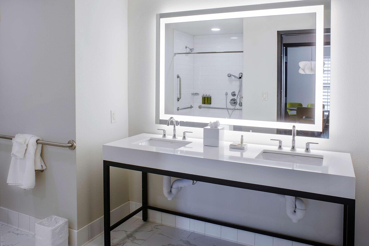 A modern bathroom with two sinks, a large mirror with backlighting, and a towel rack.