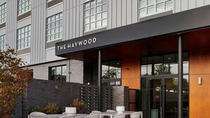 Un espace extérieur aménagé avec des tables et des chaises, un foyer et un bâtiment sur lequel est apposée une enseigne indiquant « THE HAYWOOD ».