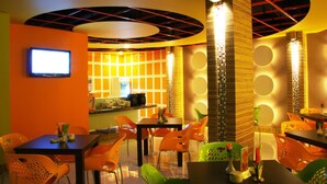 Un ristorante con pareti arancioni, una televisione a parete e diversi posti a sedere, tra cui sedie arancioni e verdi.