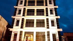Un hotel a più piani con un cartello 'Maximillian' ben visibile al piano terra, caratterizzato da un ingresso piastrellato e un ristorante con insegna.