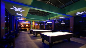 Zona biliardo con illuminazione a soffitto e un bar sullo sfondo.