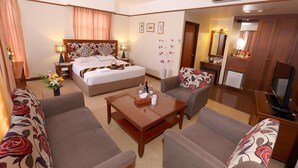 Una camera d'albergo con un letto, due divani, un tavolino, una TV e un bagno visibile attraverso una porta aperta.