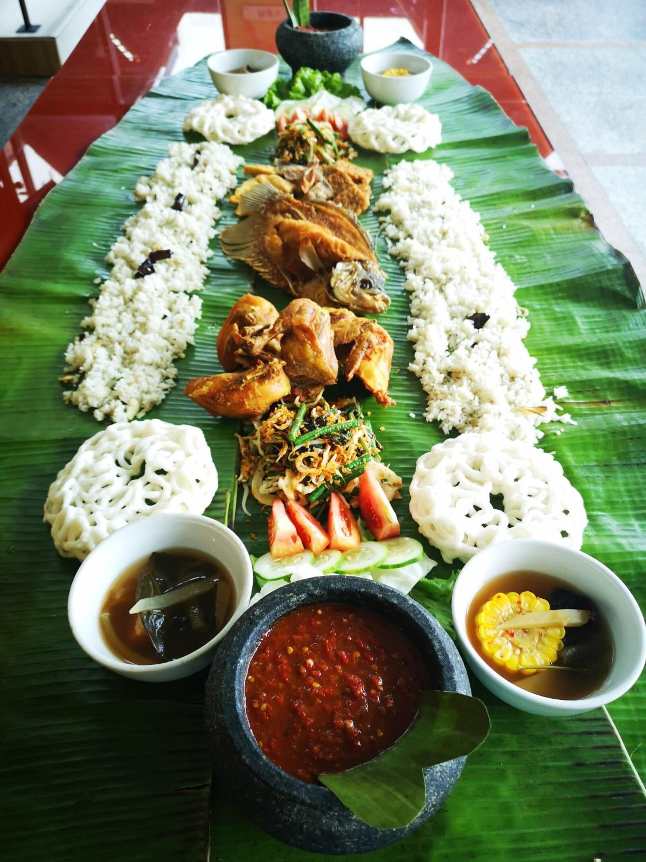 Un plat traditionnel servi sur une feuille de bananier, composé de riz, de poisson, de légumes et de diverses sauces.