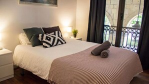 A neatly made bed with a striped blanket and patterned pillows, a bedside lamp, and a view of a balcony with a railing. - Spacious, Central and Authentic Family Apartment (Donostia)