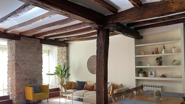 A rustic interior with exposed wooden beams, a stone pillar, a yellow armchair, a beige sofa, and a wooden dining table with chairs. - Spacious, Central and Authentic Family Apartment (Donostia)