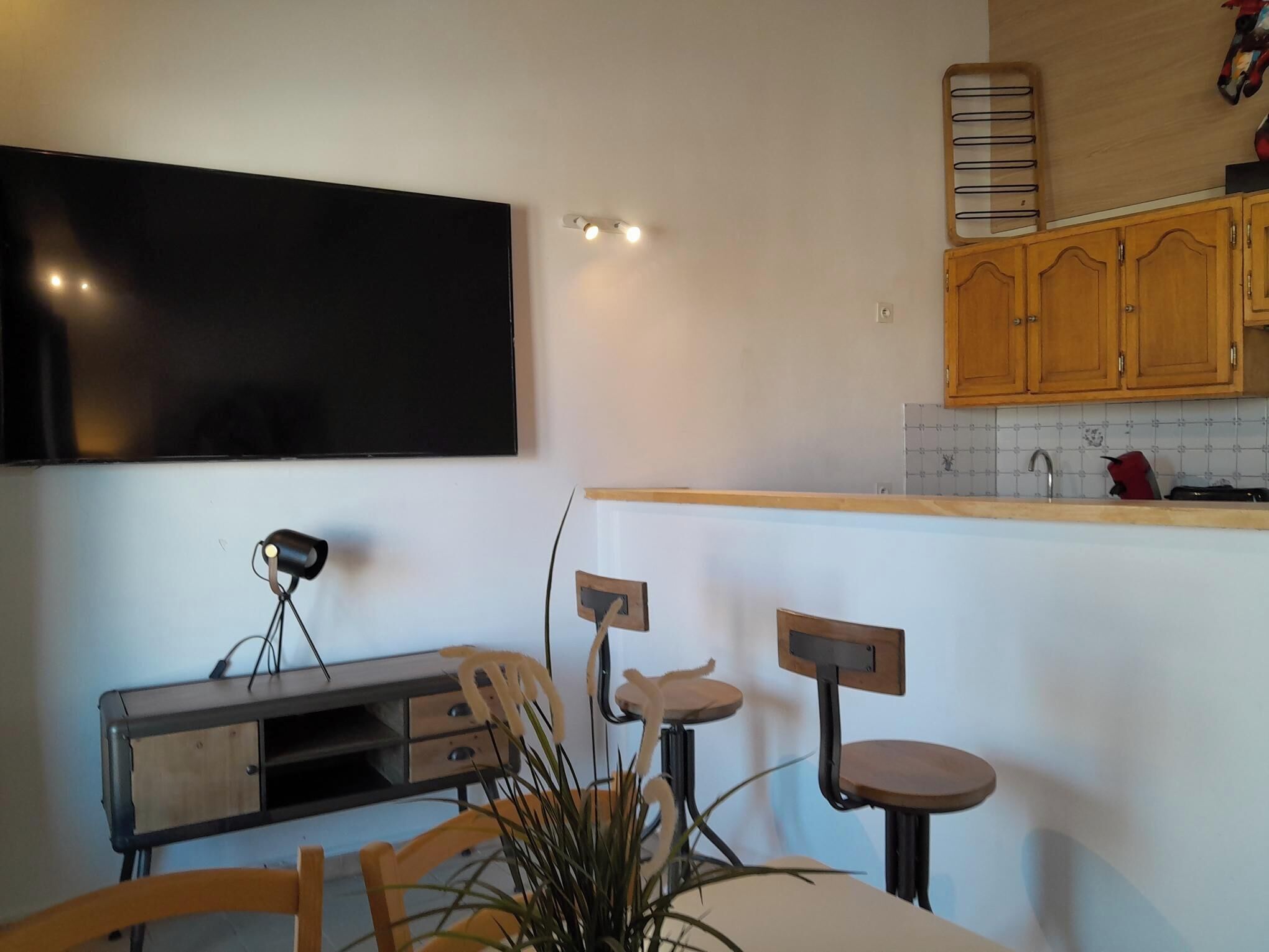 Uma cozinha moderna com televisão de tela plana, armários de madeira, bancada com pia e área de jantar com mesa e cadeiras.