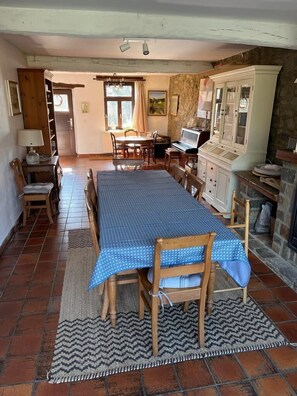 A dining area with a large table, chairs, a piano, and a stone fireplace.