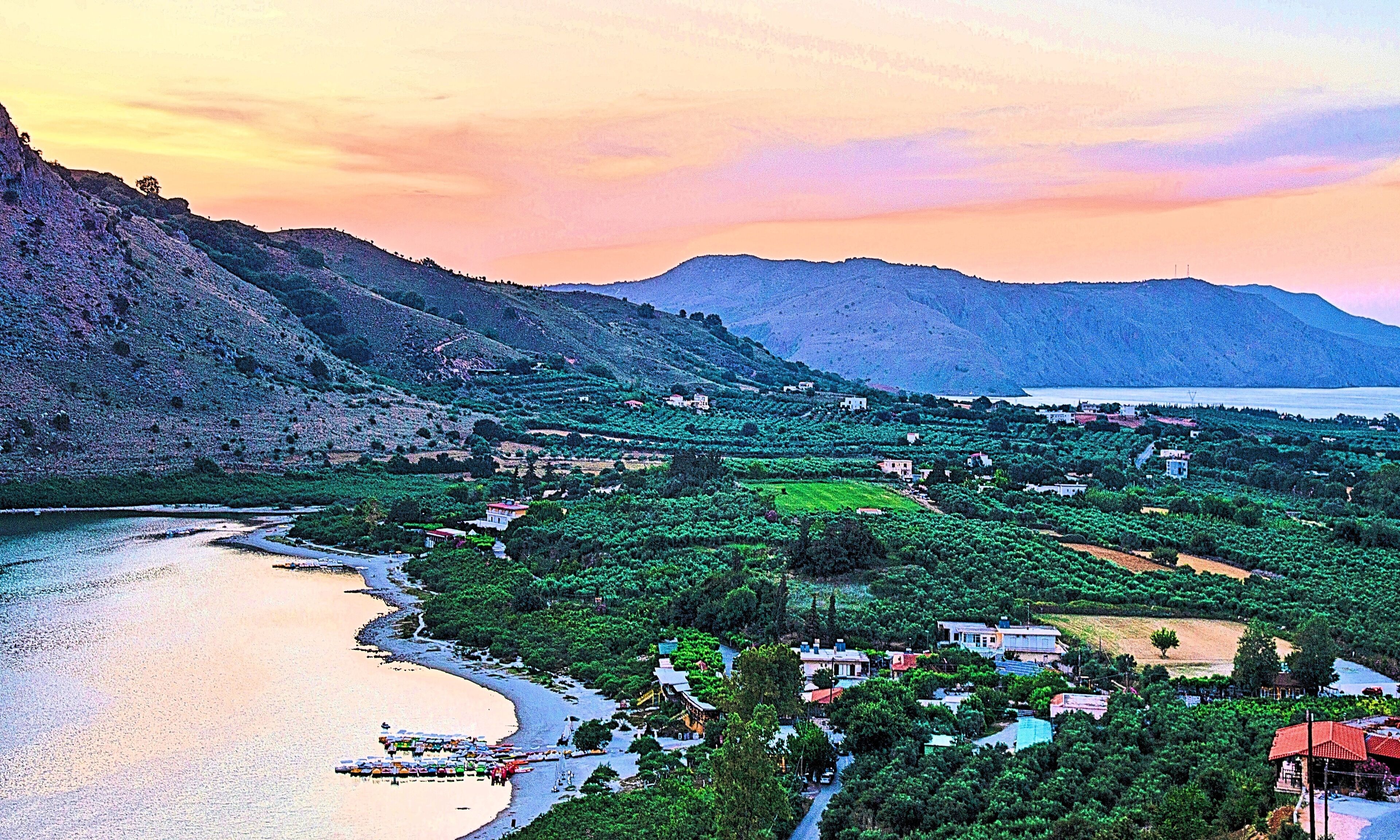 Un villaggio costiero con campi a terrazze, una spiaggia e montagne sullo sfondo.