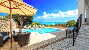 Uma área à beira da piscina com espreguiçadeiras, uma mesa e um guarda-sol.