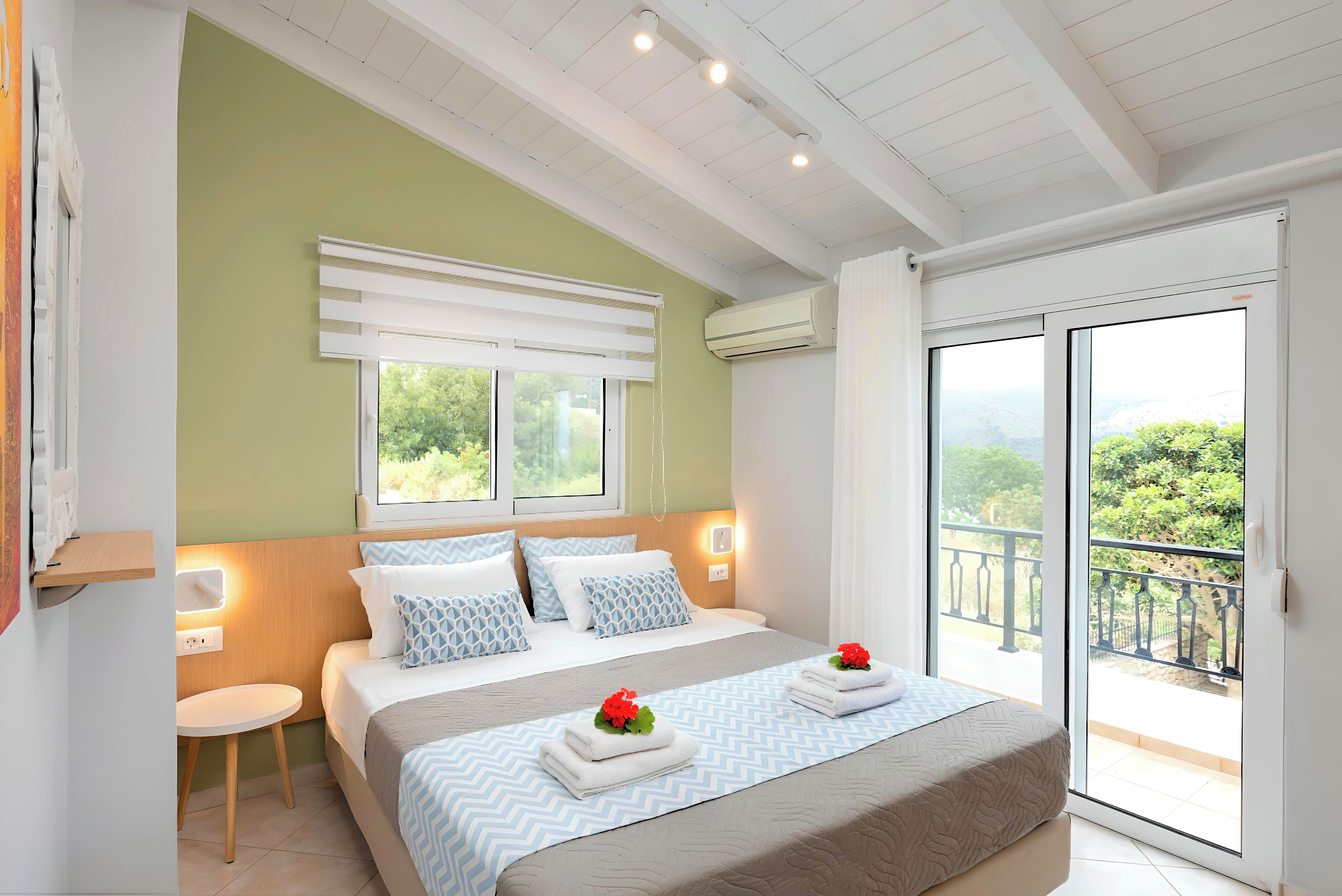 A hotel room with a bed, bedside table, and a view of the outdoors.