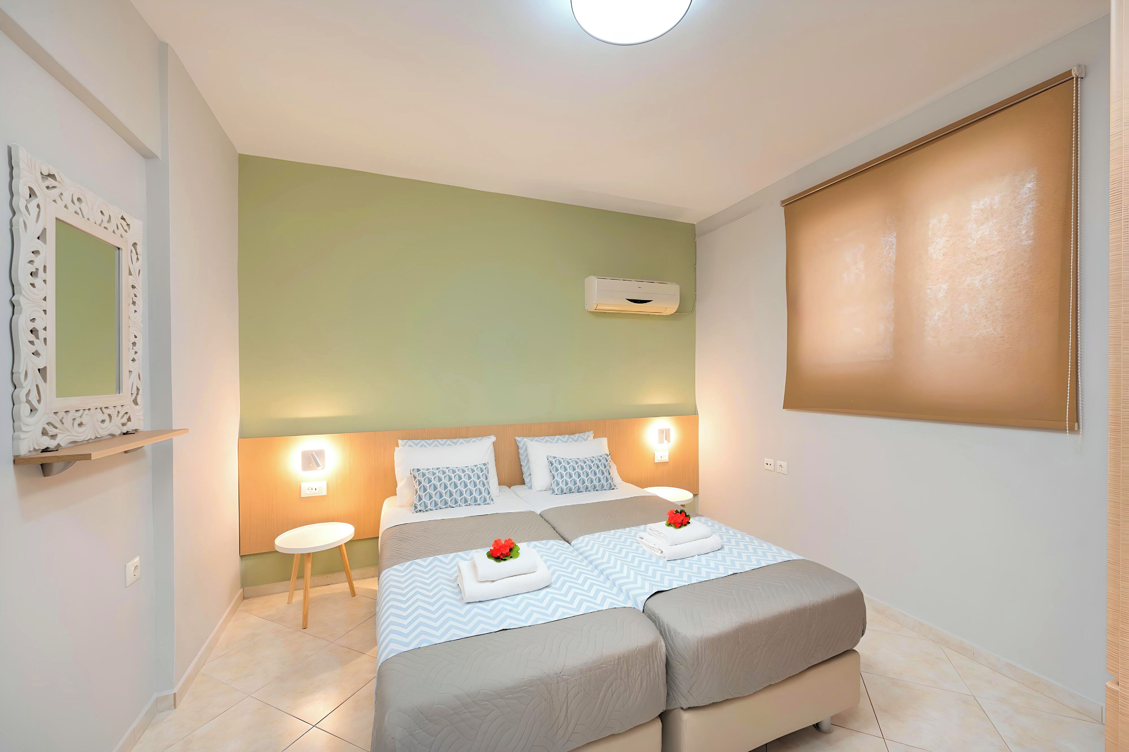 A hotel room with two beds, a bedside table, a mirror, and a wall-mounted air conditioner.
