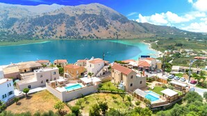 Uma vila costeira com edifícios, uma piscina e vista para o mar e as montanhas.