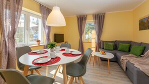 A dining area with a round table set for four, surrounded by chairs. There is a sofa and a small table with a fruit bowl on the right. - Vacation in Saxon Switzerland (Pirna OT. Graupa)