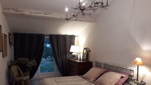 A bedroom with a bed, a nightstand, a lamp, a chair, and a window with curtains. - Charming and quiet cottage (Aix-en-Provence)