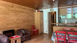 A cozy room with a wooden ceiling, a fireplace, a sofa, a dining table with chairs, and a kitchen area with cabinets and a microwave. - Spacious 6-person apt. with balcony and direct piste access (Pra-Loup)