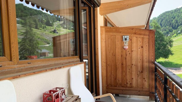 A wooden balcony with a view of a green landscape, a white chair, and a small table with boxes and a bowl. - Spacious 6-person apt. with balcony and direct piste access (Pra-Loup)