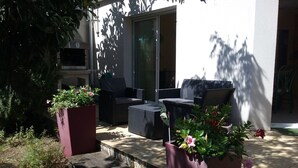 Eine Terrasse im Freien mit Korbmöbeln, Blumentöpfen und einer Glastür, die zu einem Innenbereich führt.