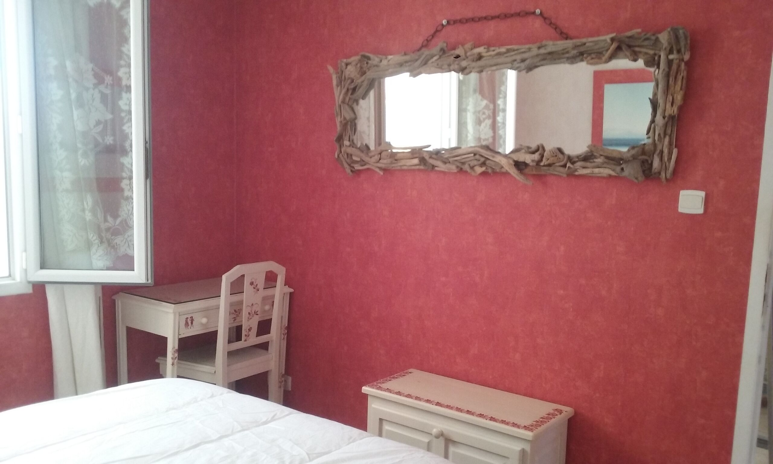 Een slaapkamer met een bed, een dressoir, een stoel en een spiegel aan de muur.