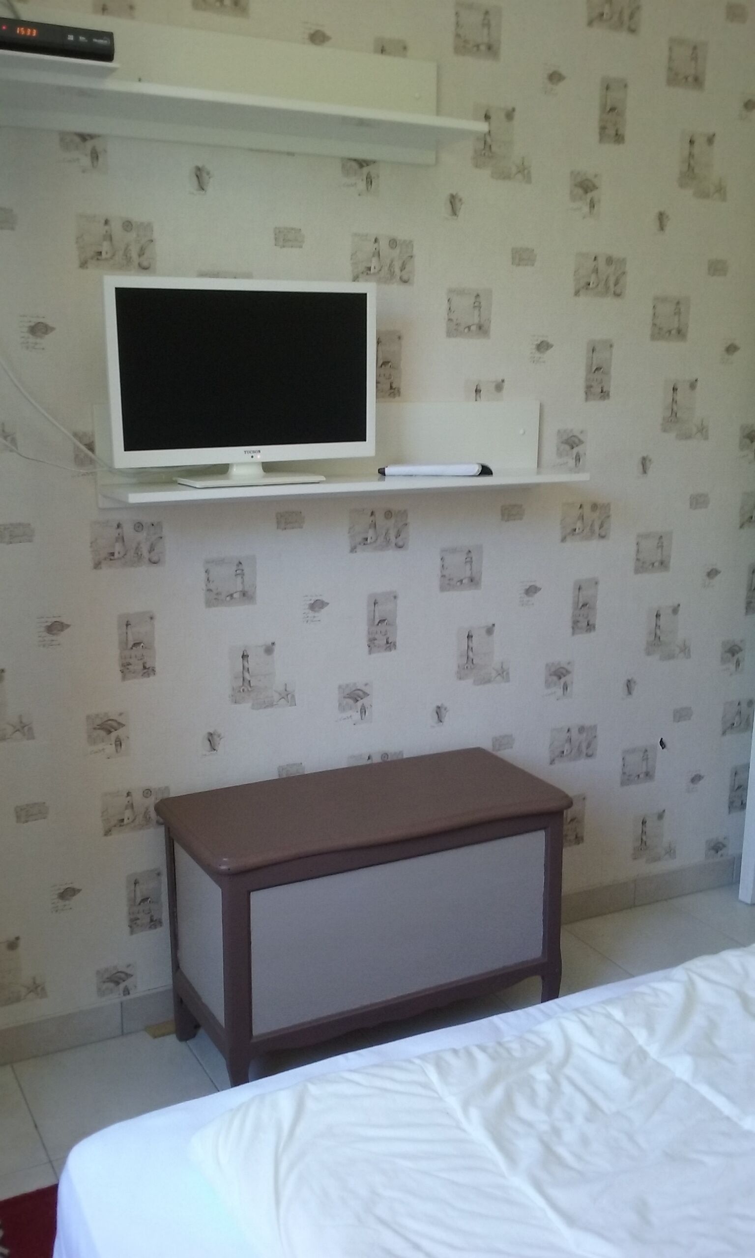 A bedroom with a bed, a TV mounted on the wall, and a small wooden nightstand.
