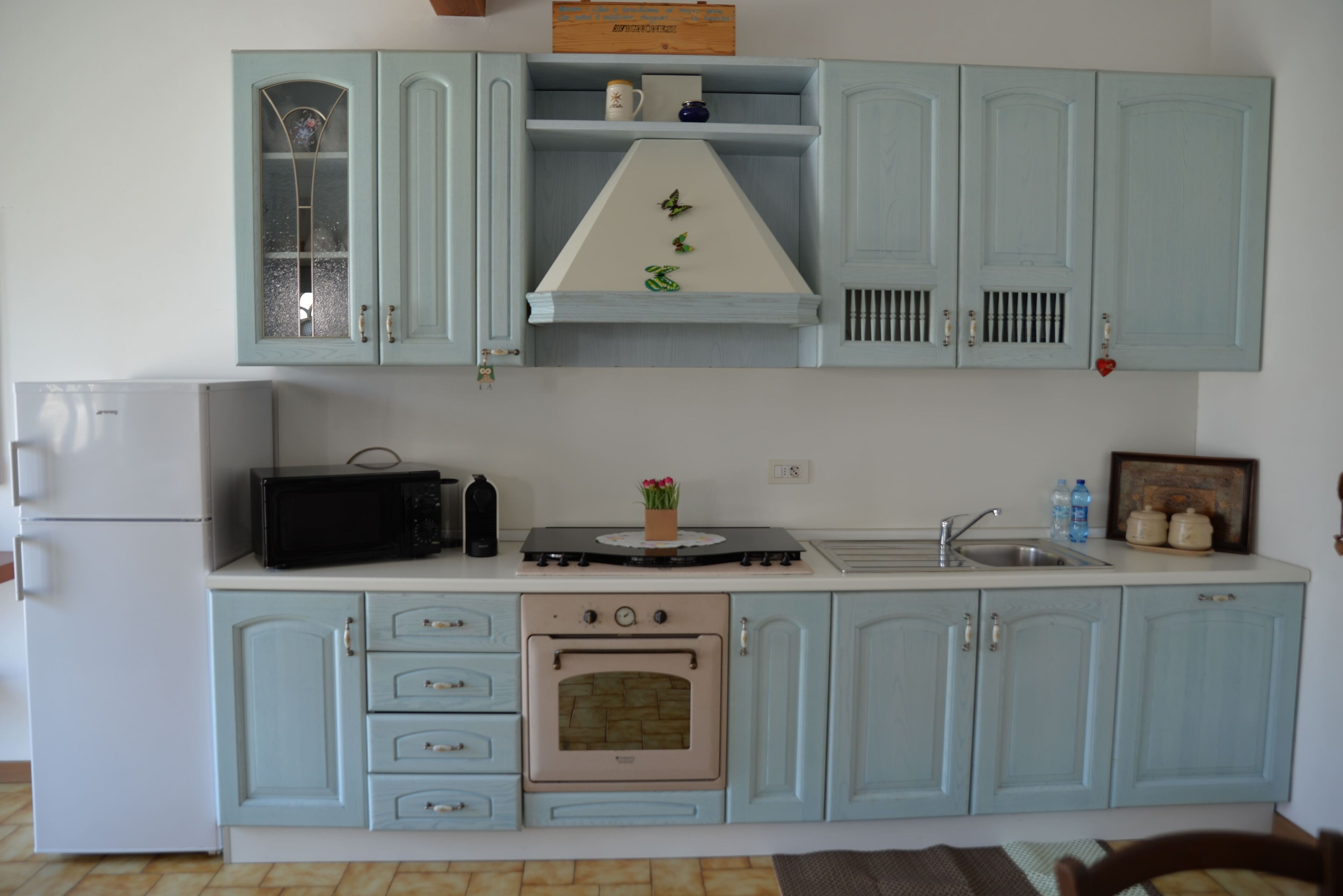 A kitchen with light blue cabinets, a stove, a microwave, a refrigerator, and a sink.