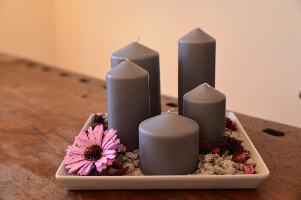 Four cylindrical candles on a square plate with a pink flower and dried petals.
