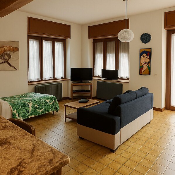 A modern living room with a sofa, a TV, a small table, and a bed with a green leaf-patterned bedspread.
