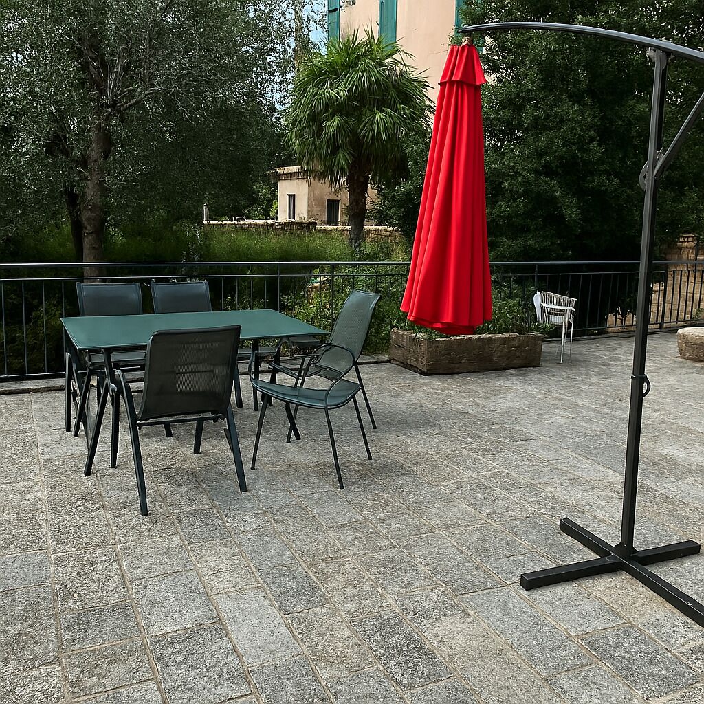 Eine Terrasse im Freien mit Tisch, Stühlen, einem roten Sonnenschirm und einem Metallständer.