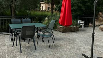 Eine Terrasse im Freien mit Tisch, Stühlen, einem roten Sonnenschirm und einem Metallständer.