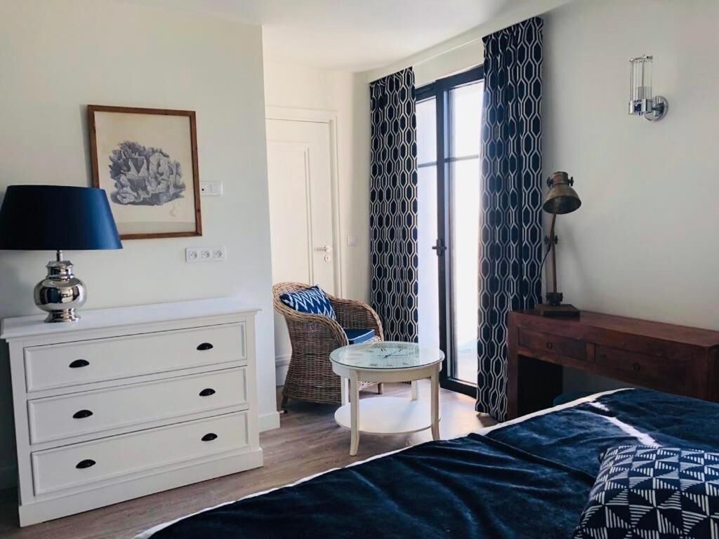 A bedroom with a bed, a dresser, a chair, a small table, and a window with curtains.