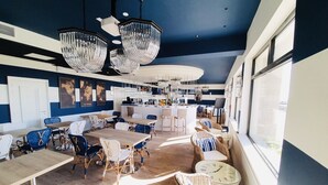 Un vaste espace dédié à la salle à manger, avec de hauts plafonds, des lustres modernes et un bar visible au fond.