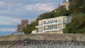 Un bâtiment situé sur la côte, doté d’un mur de soutènement en pierre et un autre bâtiment moderne avec des balcons.