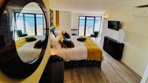 Une chambre d’hôtel équipée d’un lit, d’une télévision, d’un bureau et d’une grande fenêtre donnant sur la mer.
