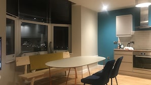 Una cocina moderna con una mesa blanca y dos sillas, un banco y una ventana con persianas.