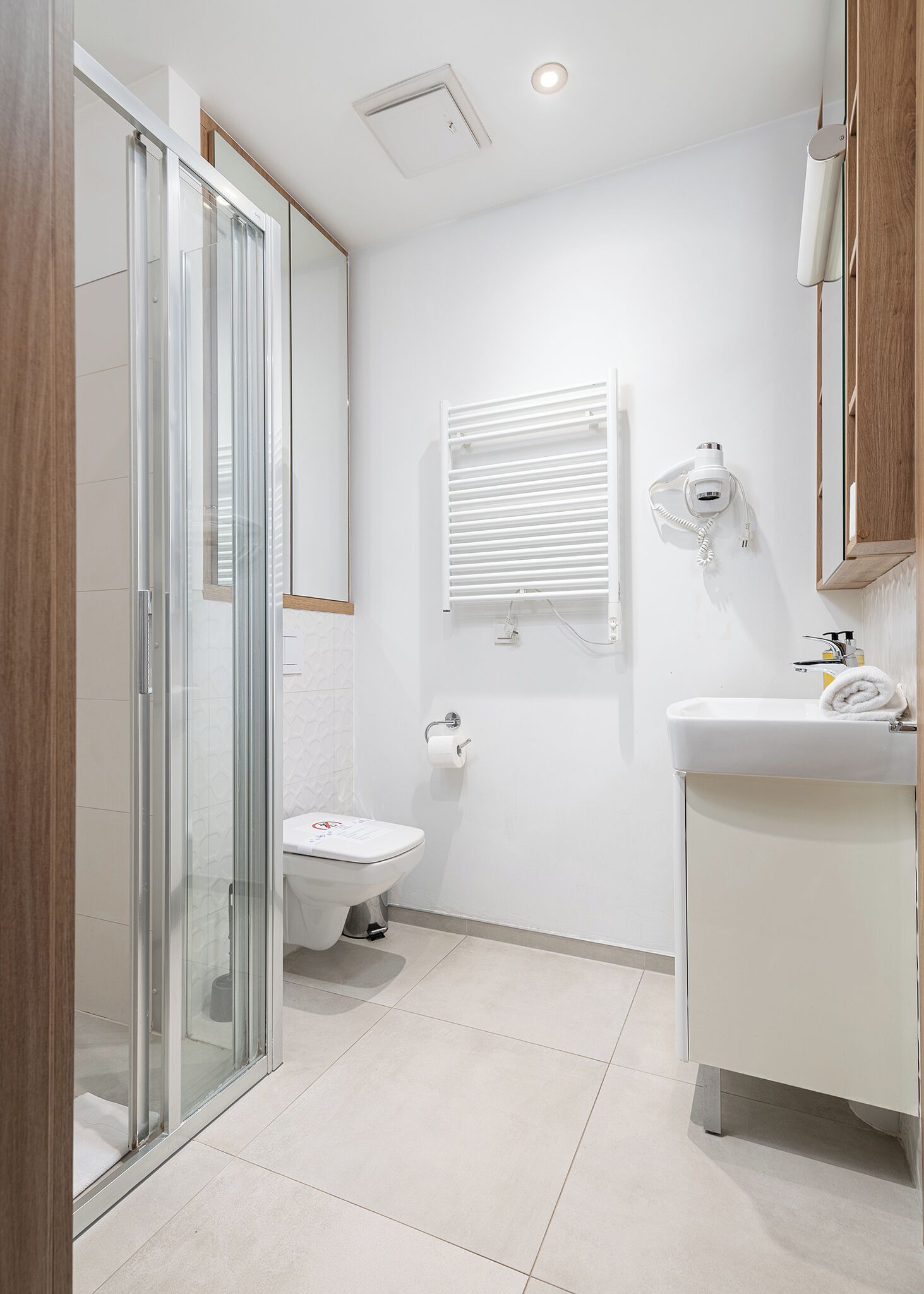 Un baño moderno con cabina de ducha de vidrio, inodoro, lavabo con toalla y secador de pelo montado en la pared.