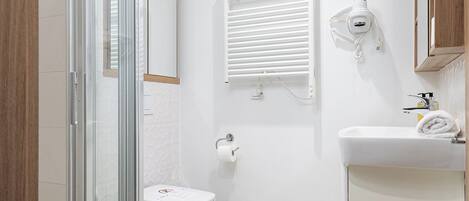 Un baño moderno con cabina de ducha de vidrio, inodoro, lavabo con toalla y secador de pelo montado en la pared.