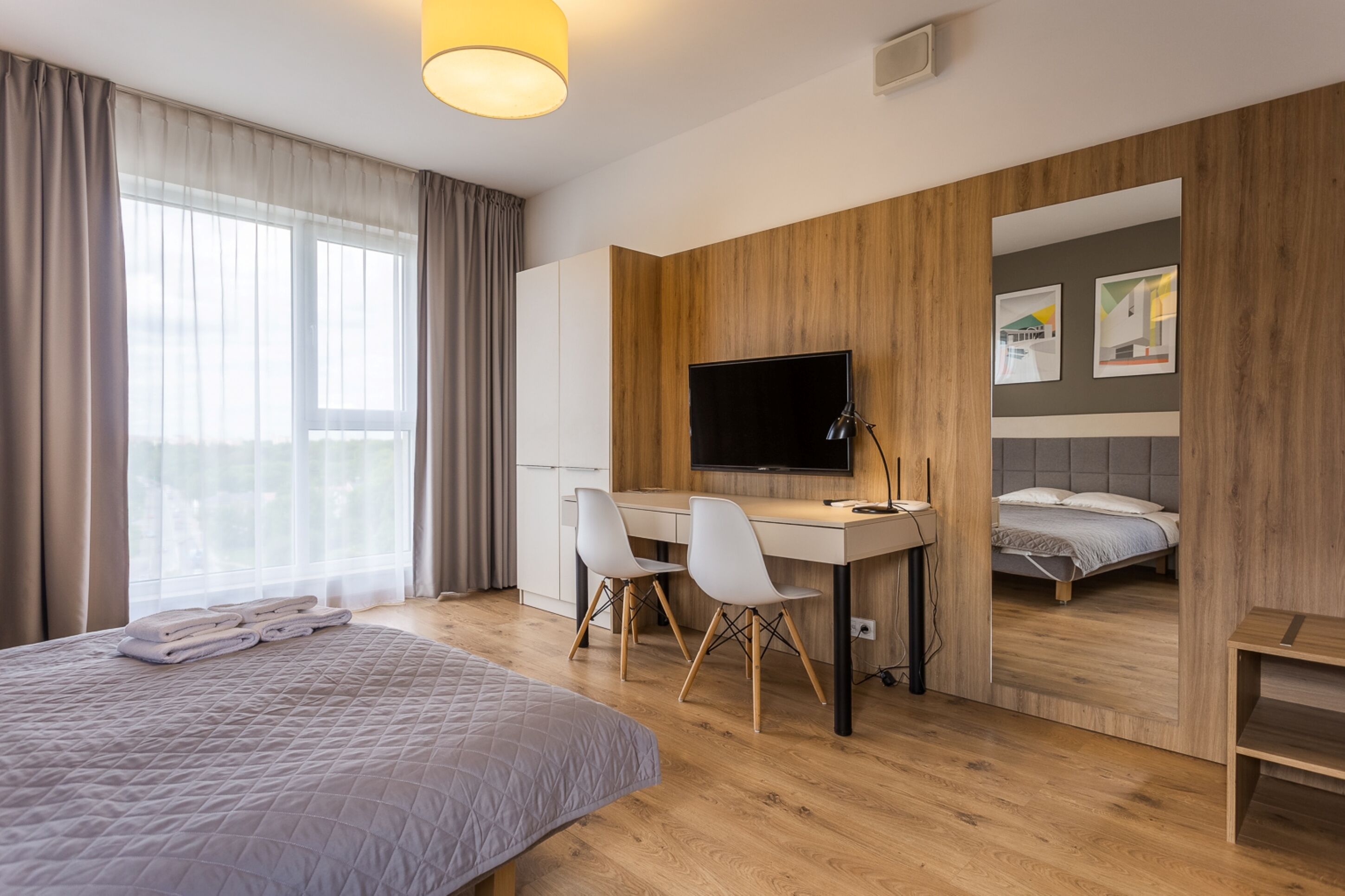 Una habitación de hotel moderna con una cama, un escritorio con dos sillas, un televisor y obras de arte en la pared.