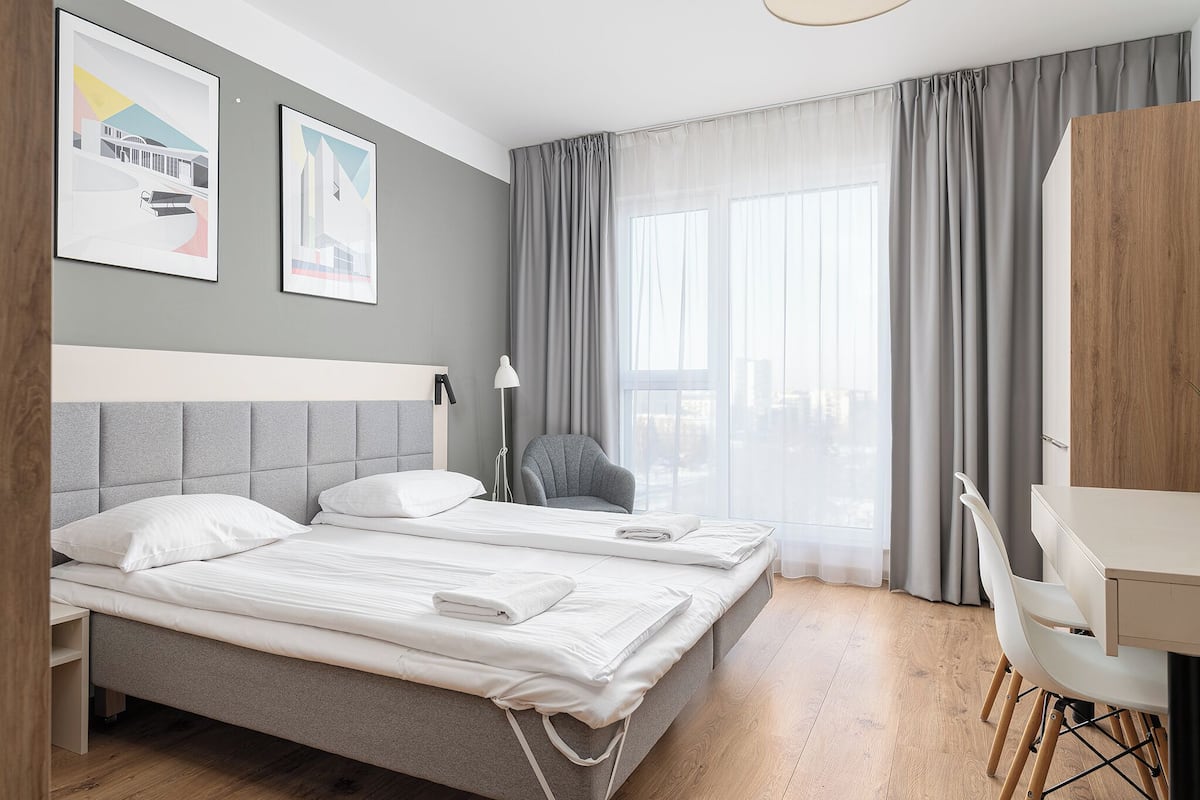 A hotel room with two beds, a desk, a chair, and a large window with curtains.