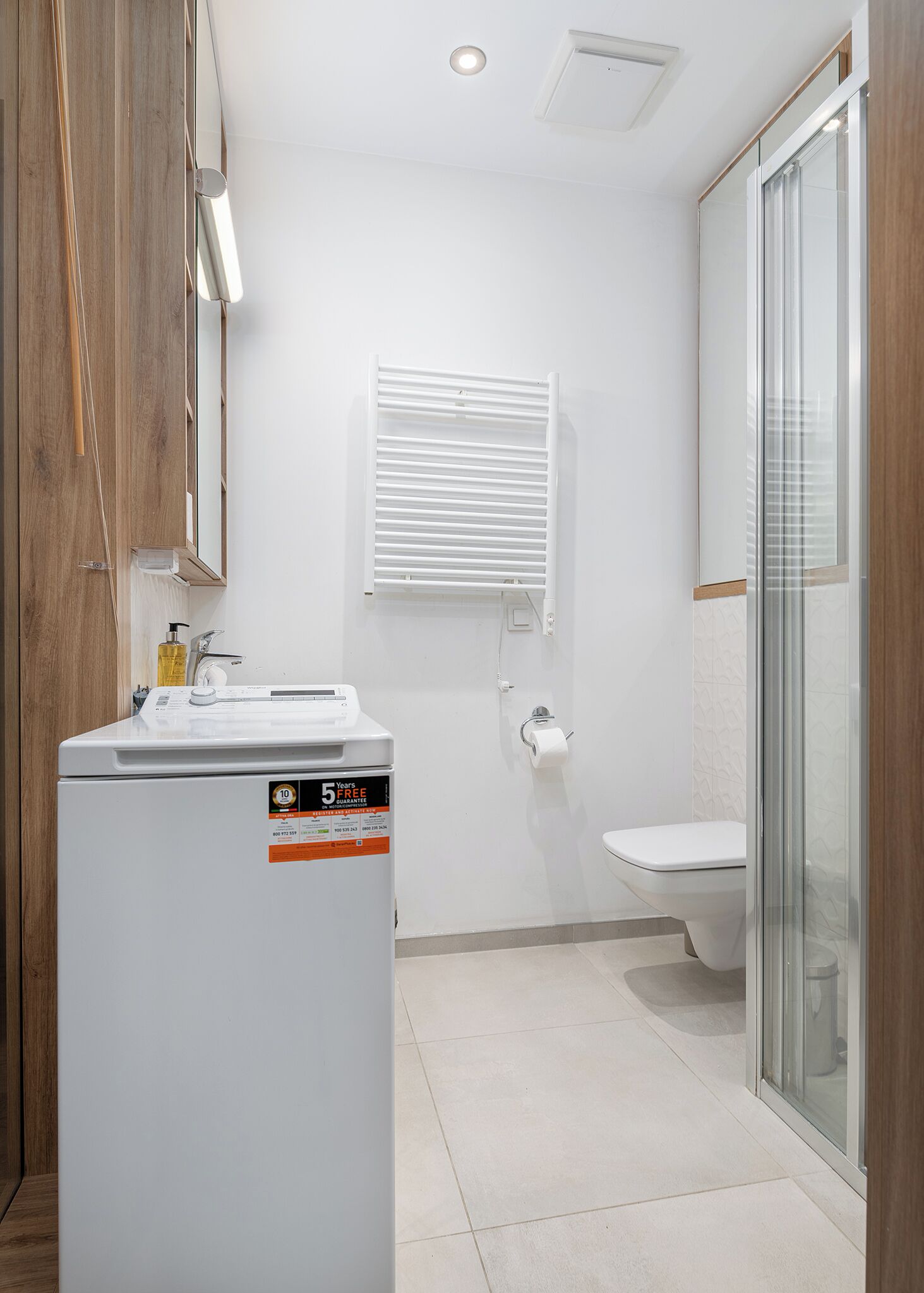 A modern bathroom with a built-in washing machine, a toilet, and a glass shower enclosure.