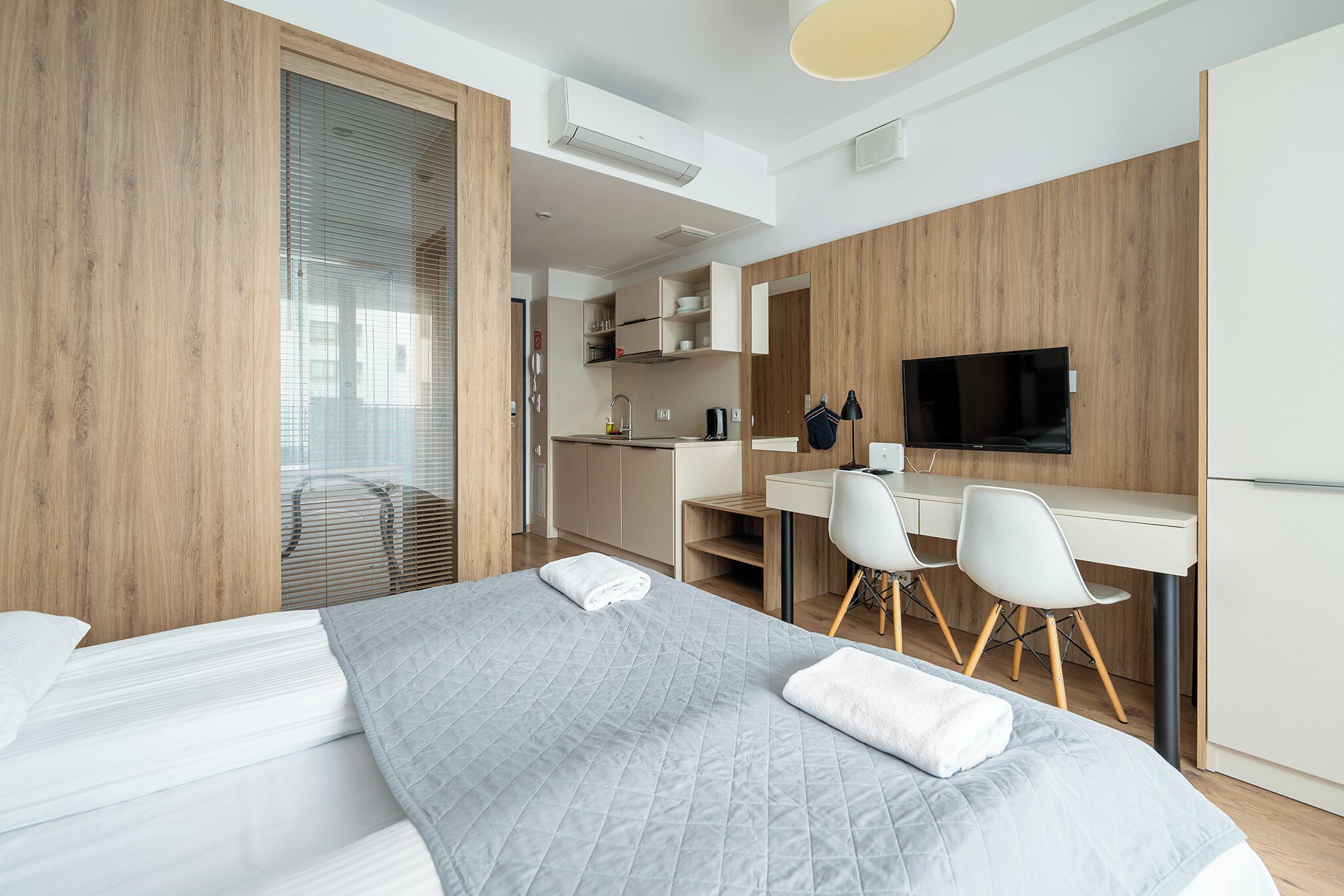 Une chambre d’hôtel moderne équipée d’un lit, d’un bureau, de deux chaises, d’une télévision et d’une kitchenette.