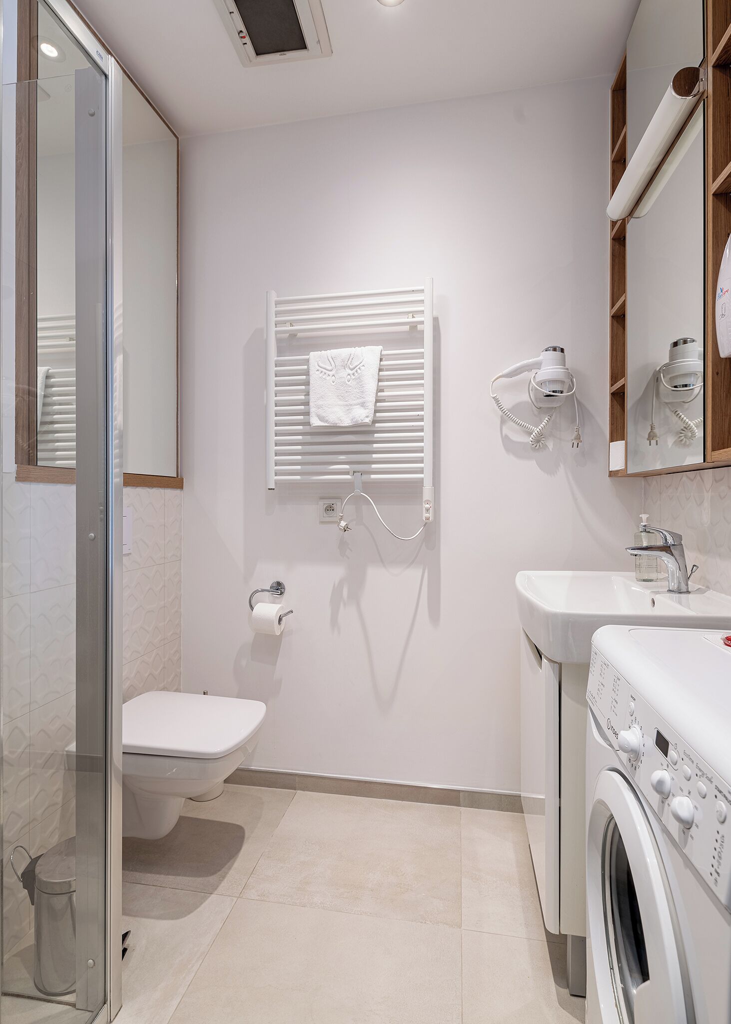 Une salle de bain moderne équipée d’une douche à parois de verre, de toilettes, d’un porte-serviettes, d’un sèche-cheveux et d’un lave-linge.