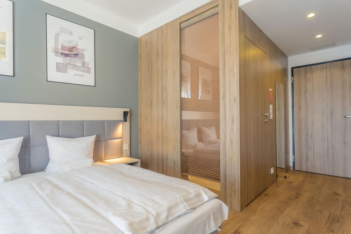 A modern bedroom with a bed, nightstands, a wooden wardrobe, and a large window with blinds.