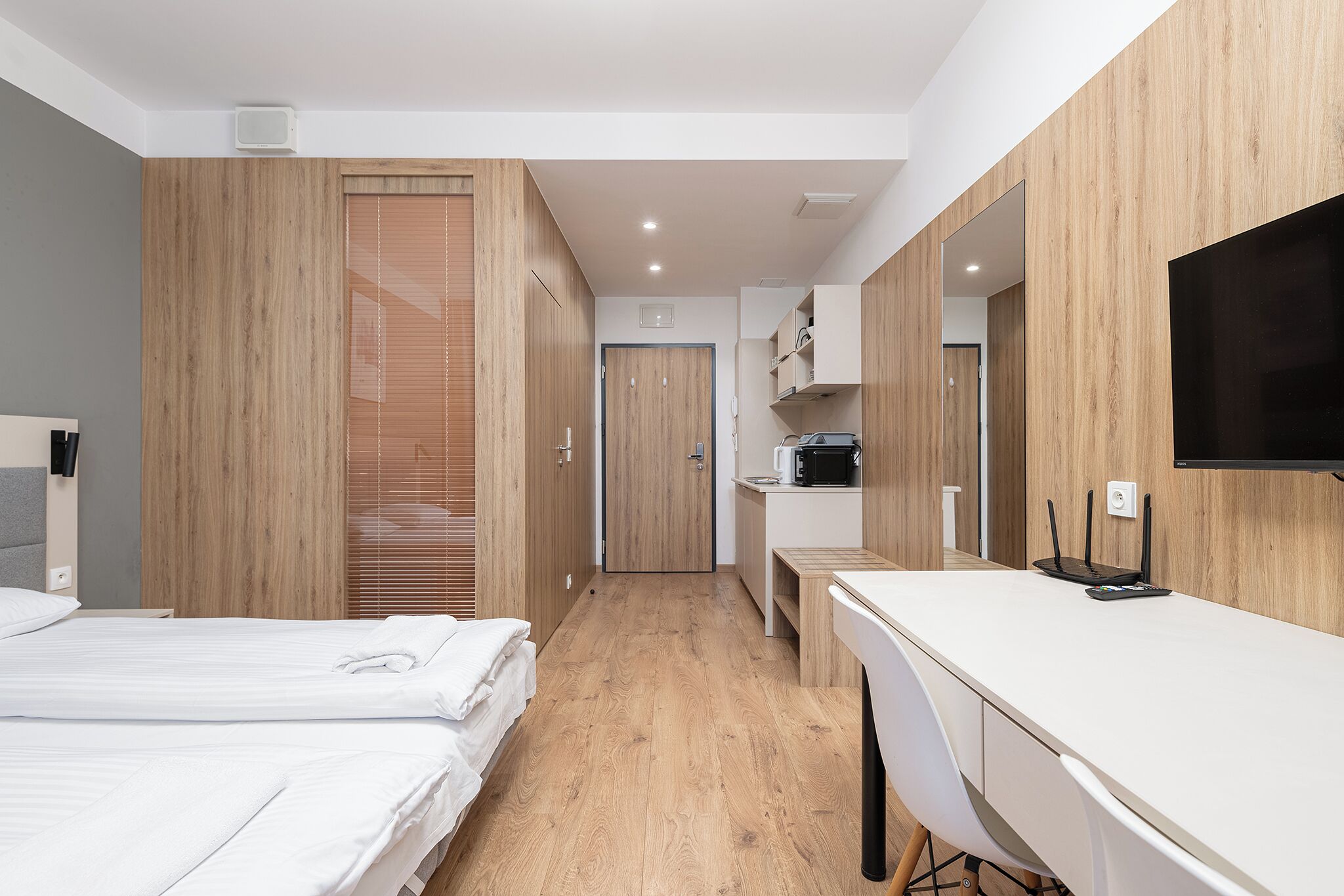 Une chambre d’hôtel moderne avec des panneaux de bois, un lit, un bureau et un téléviseur à écran plat.