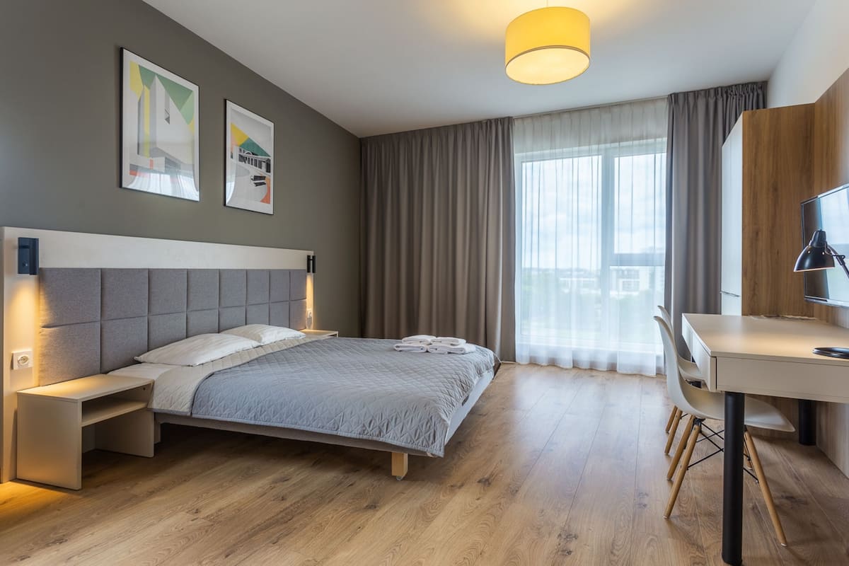 A modern hotel room with a bed, bedside table, desk, and chair.