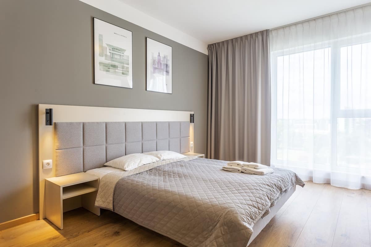 A modern bedroom with a large bed, a bedside table, and a headboard. There are two framed pictures on the wall above the bed.