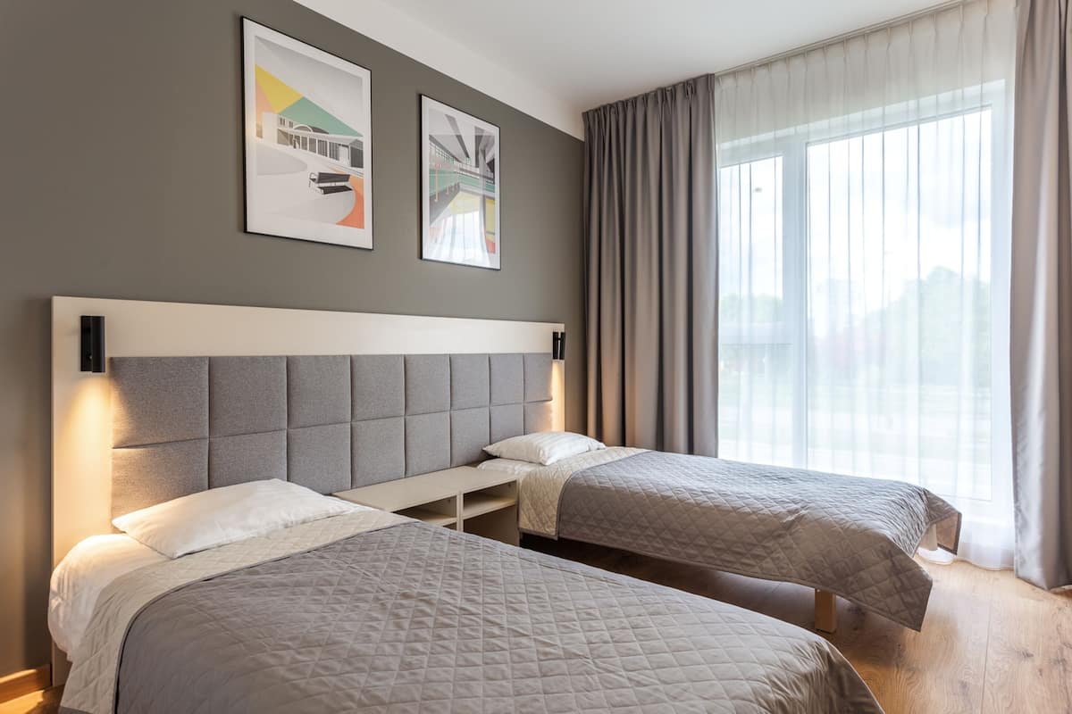 A hotel room with two beds, a large window with curtains, and artwork on the wall.