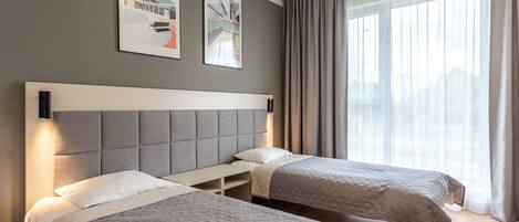 A hotel room with two beds, a large window with curtains, and artwork on the wall.