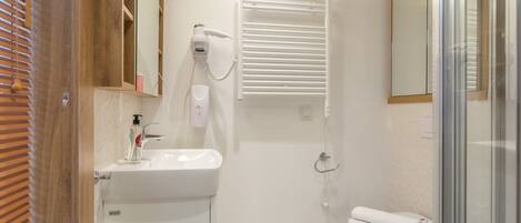 A bathroom with a white sink, a mirror, a hairdryer, a towel, and a glass shower enclosure.