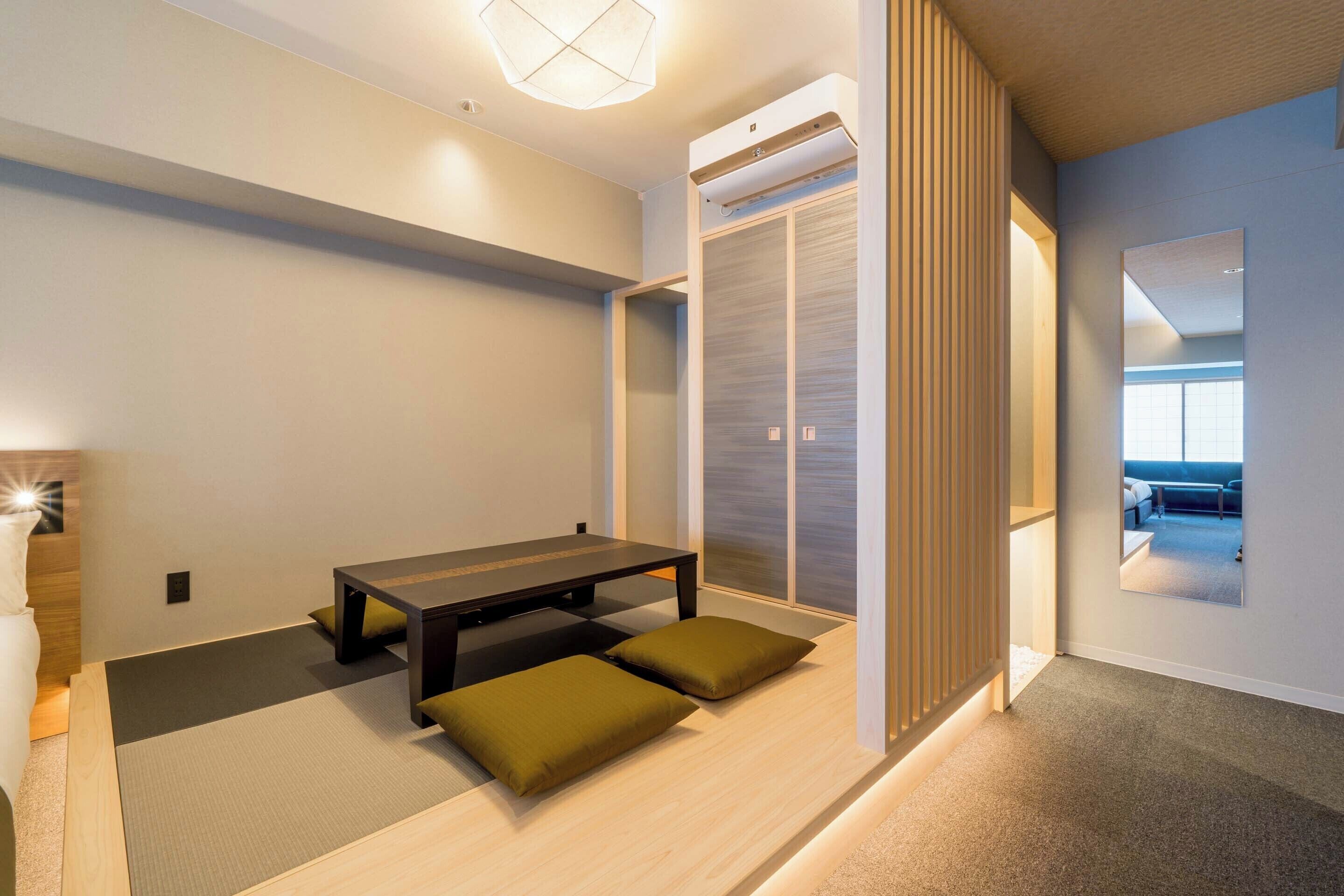 A modern hotel room with a wooden floor, a dining table with cushions, a sliding door, and a large mirror.