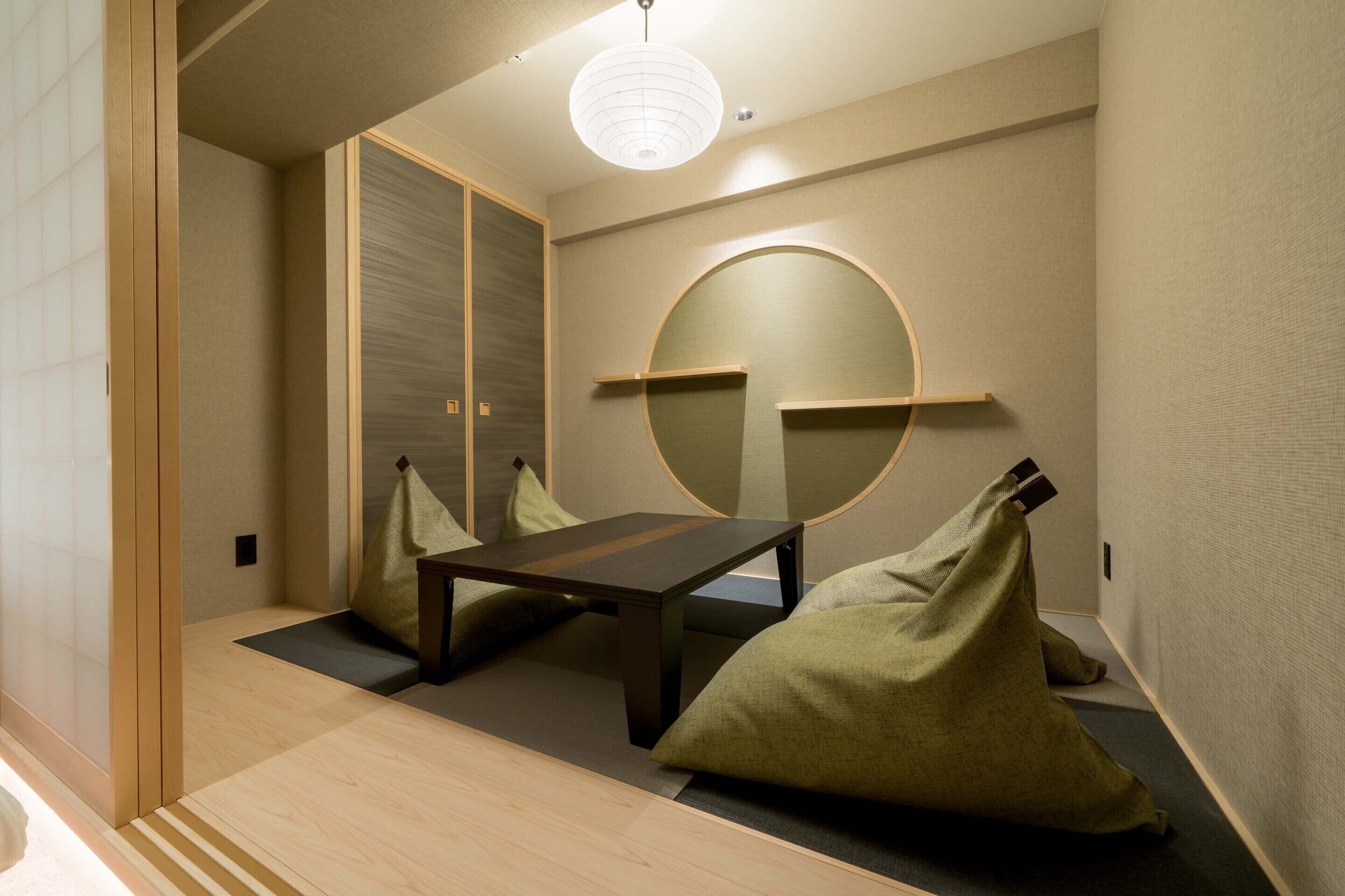 Una habitación con suelo de tatami, una mesa baja, cojines y un espejo circular montado en la pared.