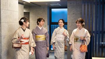 A group of people in traditional Japanese kimonos walking through a modern hotel lobby with stone walls and a blue-toned background.